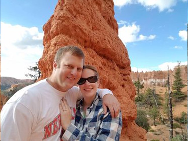 A man and a woman embrace along a trail near red rock spires